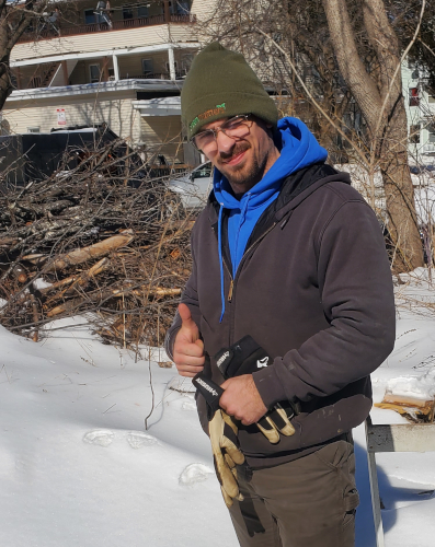 Owner of Debris Dragon giving a thumbs up in front of a pile of brush